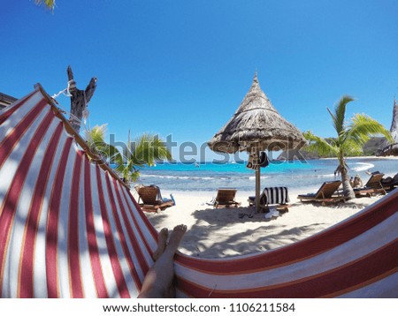 Woman relaxing and sunbathing in the red and white hammock on the beach with her feets up. Turquoise sea water, sunny day, palm trees. Travel/holiday/vacation careless atmosphere. Summer activity.
