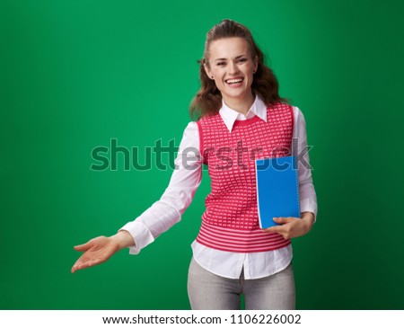 smiling modern student woman in a red waistcoat with a blue notebook welcoming against green background