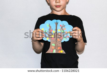 A smiling boy holds a cartoon autumn fall tree in his hands
