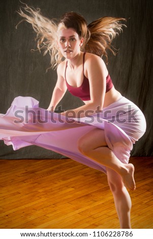 Full length studio shot of beautiful young dancer in burgundy top and lavender skirt, turning rapidly with hair flying while dancing in the studio.