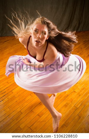Full length studio shot of beautiful young dancer in burgundy top and lavender skirt, turning rapidly with hair flying while dancing in the studio.