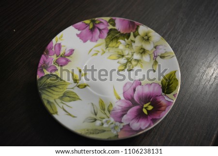 Ceramic saucer multi-colored with a white border and flowers on a brown wooden brown background