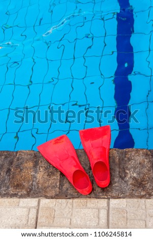 Red rubber flippers on the side of the blue swimming pool. Bright beach accessories on pool background