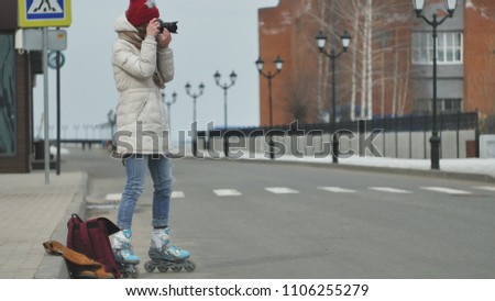 Young beautiful woman in red hat wearing sporty warm clothes and rollers, sitting on the asphalt road and taking pictures on a vintage camera 4k