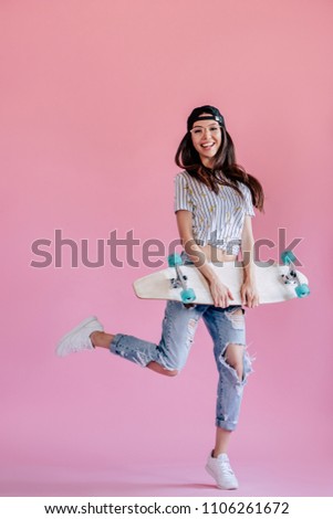 Young asian teenage girl on pink background. Stylish young woman with skateboard isolated.