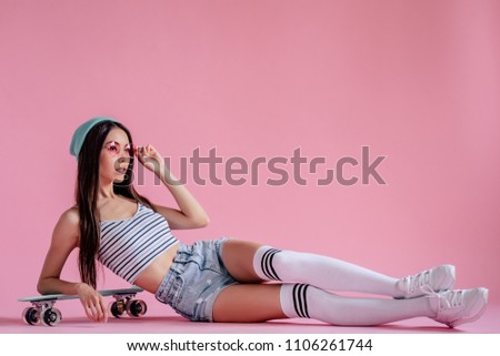 Young asian teenage girl on pink background with pink glasses. Skater girl in shorts with skateboard isolated.