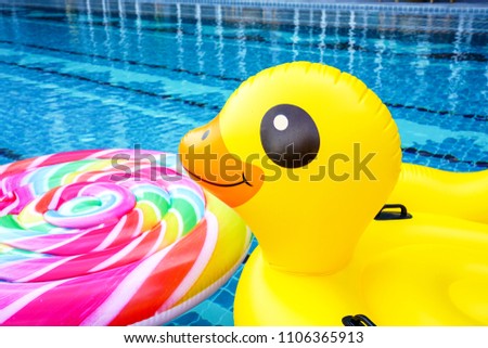 Inflatable toy duck and lollipop float on blue bright swimming pool. Idea for summer fun party concept.