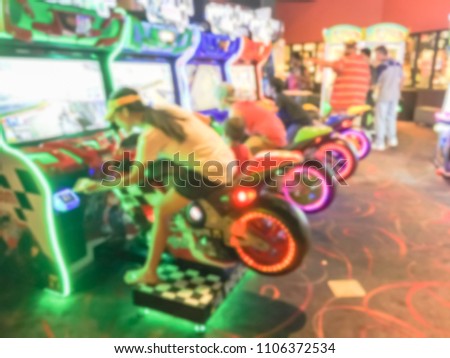 Abstract blurred dark room at entertainment complex in America, motion blurry arcade area with player on motorcycle racing simulator arcade game