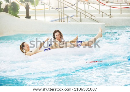 Two girls in an aquapark on a rubber ring laughing happily skate on water slides splashing water and sun