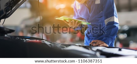 car service, repair, maintenance concept - Asian auto mechanic man or Smith writing to the clipboard at workshop warehouse, technician doing the checklist for repair machine a car in the garage,banner Royalty-Free Stock Photo #1106387351