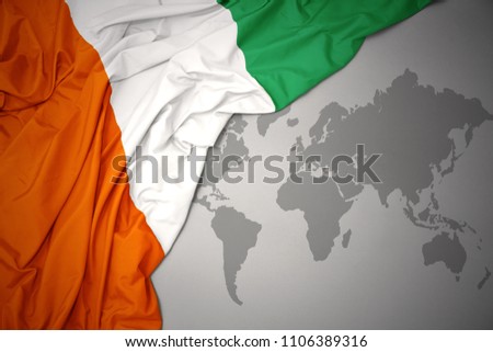 waving colorful national flag of cote divoire on a gray world map background.