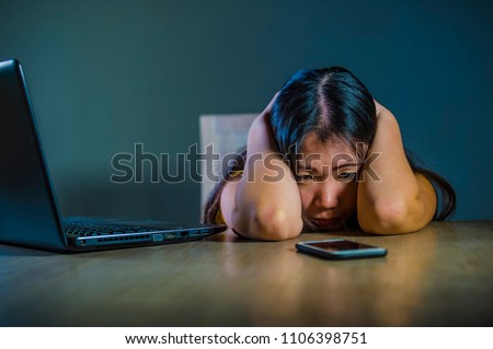 dramatic portrait scared and stressed Asian Korean teen girl or young woman with laptop computer and mobile phone suffering cyber bullying stalked and harassed with internet password hacked Royalty-Free Stock Photo #1106398751