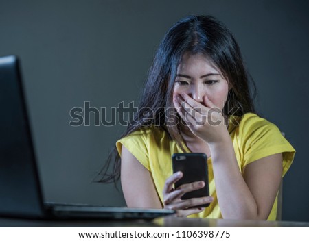dramatic portrait scared and stressed Asian Korean teen girl or young woman with laptop computer and mobile phone suffering cyber bullying stalked and harassed with internet password hacked