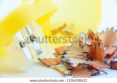 High resolution shot of pencil shavings with a double blade sharpener and trash container / a bin on white paper. Pencil shavings is wood fiber that is carved or peeled off to expose the graphite core