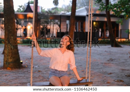 Young girl riding swing on sand, houses in background. Concept of leisure, summer vacations and resort.