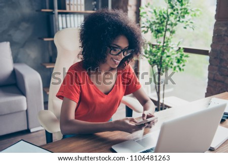 Portrait of cheerful trendy secretary sitting at desktop on armchair holding smart phone in hands using 5G wi-fi internet chatting with friends checking email searching contact enjoying free time Royalty-Free Stock Photo #1106481263