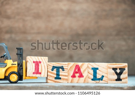 Yellow toy forklift hold letter block T to complete word Italy on wood background