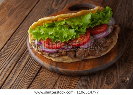 Delicious fresh homemade sandwich with chicken burspit roasted meat, tomato, onions and lettuce on wooden board on dark wooden rustic table. Doner kebab. Healthy food concept.