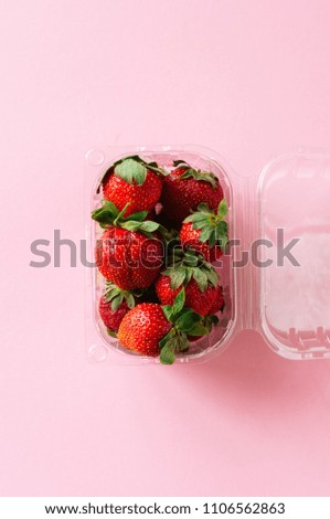 Fresh ripe strawberries in plastic container on a light pink background. Top view and copy space. Organic food concept.