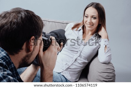 Professional photo shoot at the studio, a female model is posing on an armchair and smiling; the photographer is taking pictures with his digital camera