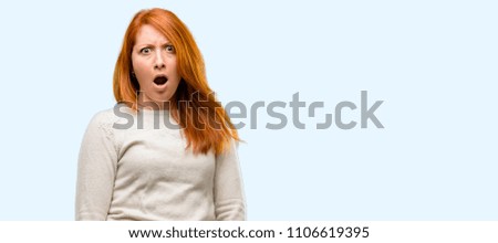 Beautiful young redhead woman scared and surprised cheering expressing wow gesture. Unbelieving isolated over blue background