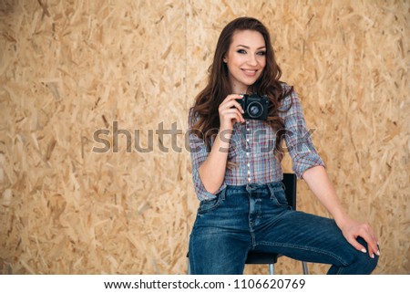 A nice and satisfying shining woman sits on a chair in everyday jeans and a shirt, she is happy, because she just made an excellent shot on her camera.