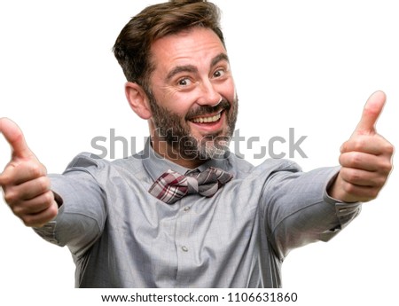 Middle age man, with beard and bow tie stand happy and positive with thumbs up approving with a big smile expressing okay gesture isolated over white background