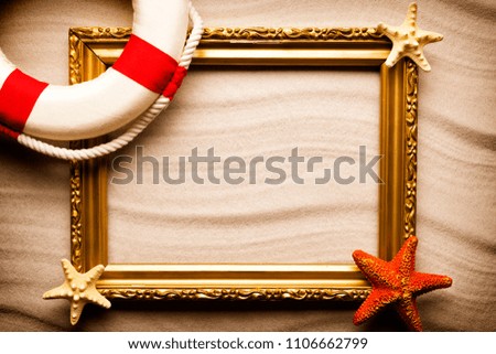 Summer background - lifebuoy, picture frame and shells on sand 