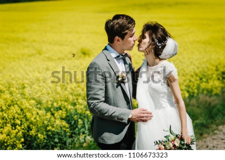 A newlywed wedding couple embrace and kissing on a straight road, country for their honeymoon. Way on summer field of yellow rapes flowers, canola field.
