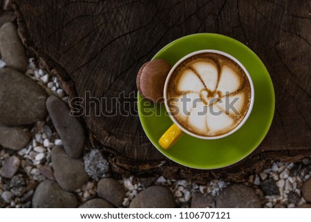 Cappuccino in a green cup with a beautiful pattern, on a wooden and stone background. Coffee art.