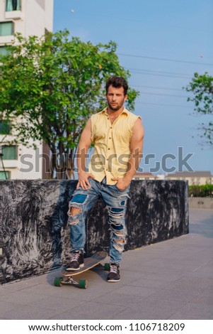 Young handsome man with beard standing with longboard on the street.