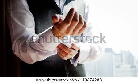 A groom putting on cuff-links as he gets dressed in formal wear .Groom's suit Royalty-Free Stock Photo #110674283