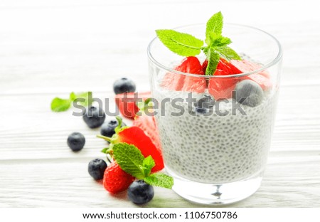 Portion of chia pudding with vegan almond milk, blueberry & strawberry, mint, served in glass. Healthy vegetarian breakfast, seeds berries, greek yogurt, wooden table. Background, close up, copy space