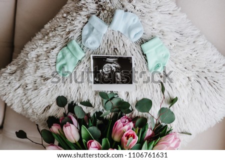 Newborn accessories: socks for a baby and ultrasound scan or picture of future daughter or son. Bouquet of flowers greetings for a party in honor of pregnant at home. Top rear view. baby shower.