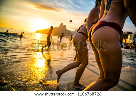 Defocused view of sunset on ipanema beach in Rio de Janeiro with two ladies in bikinis and guys playing beach soccer with two brothers mountain backdrop