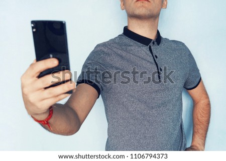 guy takes himself on a mobile phone. A young man takes a selfie. a man reading SMS on a black smartphone. A person looks into the phone screen on blue background