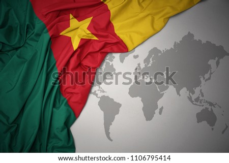 waving colorful national flag of cameroon on a gray world map background.