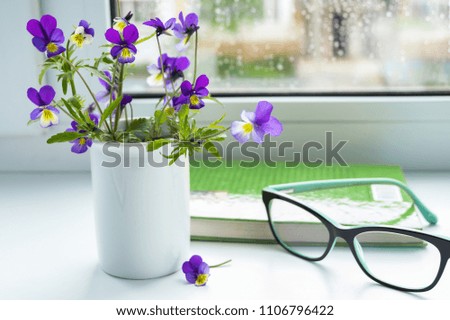Wildflowers, book and glasses on the window in rainy weather.