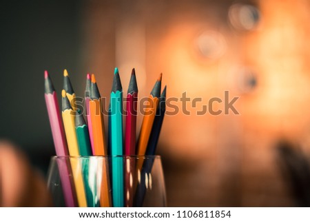Colourful pencils in a glass jar against orange light blurry background. Warm tone filter effect. Copyspace