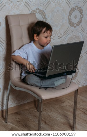 the boy is sitting on a chair and is holding a laptop
