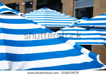 Close up on a blue and white stripe beach umbrella, at an outdoor patio and sitting area, with space for text on top