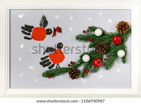Prints of the hands palms are stylized as bullfinches. Branch of fir tree with cones, red apples and white balls. Handmade picture in a frame as an illustration of a New Year or Christmas holiday