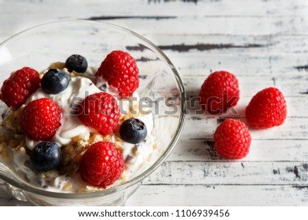Raspberries, blueberries, cereals and yogurt in a glass bowl on wooden slats. Healthy breakfast for a healthy life. Horizontal image.