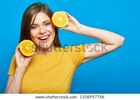 Cheerful girl holding two slices of orange. Blue wall background.