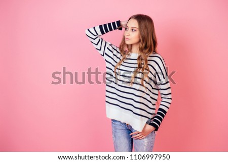 portrait of a young and attractive teenager long-haired woman stylish model posing in a striped sweater in studio on a pink background