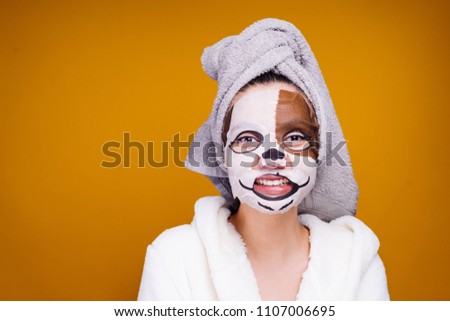 funny young girl with a towel on her head and in a white bathrobe after a shower smiles, on her face a mask with a dog's face