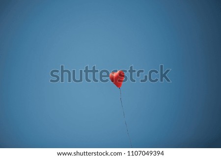 Red balloon in form of heart on background of blue sky