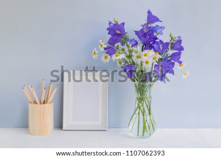 Mockup with a white frame and summer blue flowers in a vase on a light blue background