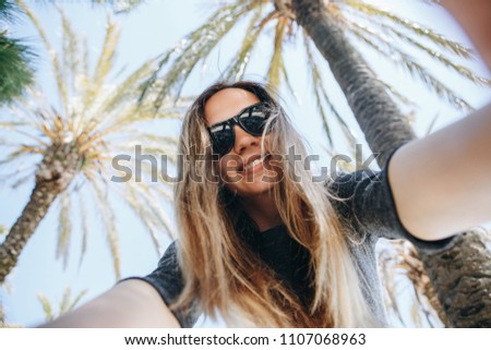 Young beautiful woman tourist or blogger makes a selfie or is reporting to its subscribers on the background of palm trees in a hot country