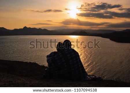 Loving couple is sitting on a cliff against the background of the sea at sunset